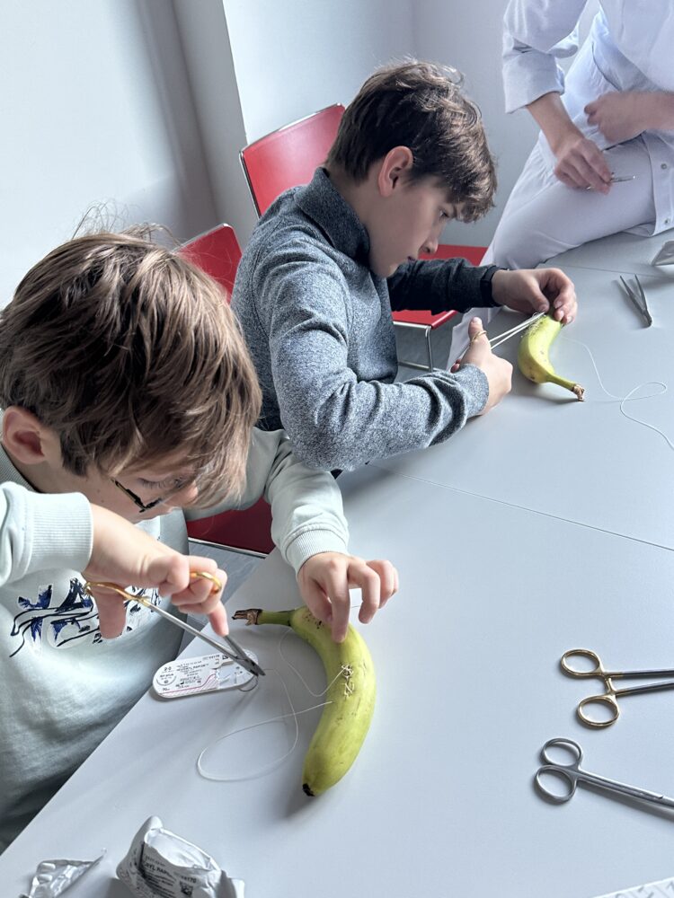 Schüler:innen üben mithilfe von Bananen mit medizinischen Geräten eine Naht zu schließen.