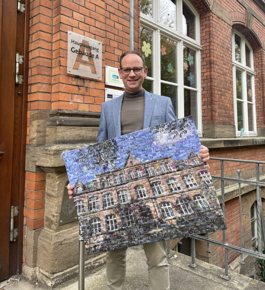 Peter Kock mit einem Abschiedsgeschenk, ein Foto des Herder-Gymnasiums auf der Treppe vor dem Schuleingang.