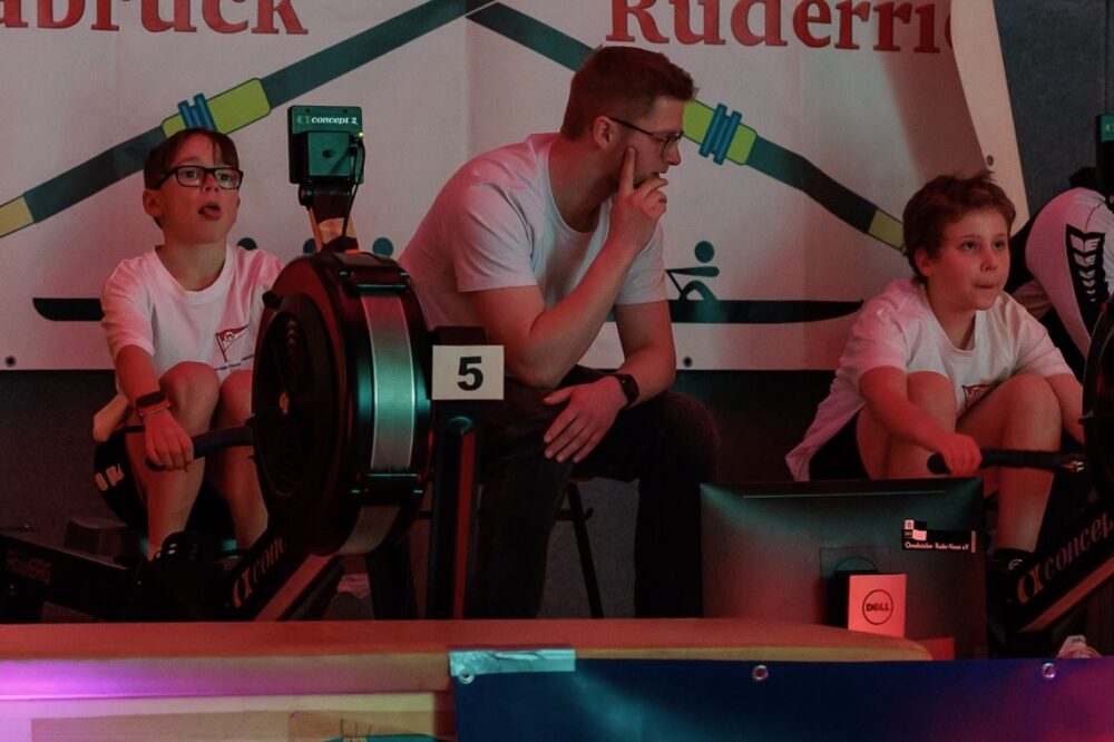 Junge Ruderer am Ergometer werden vom Trainer unterstützt