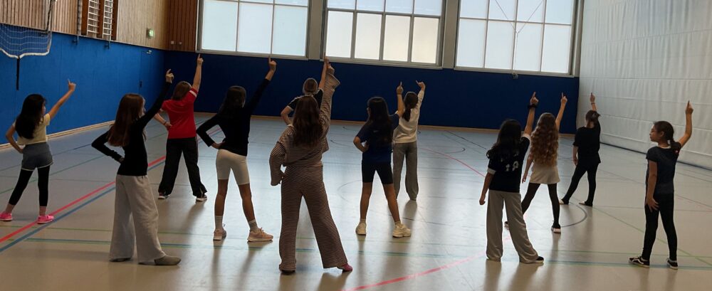 Die Mädchen der Tanz-AG stehen in drei Reihen und strecken den rechten Arm mit dem Zeigefinger in die Luft.