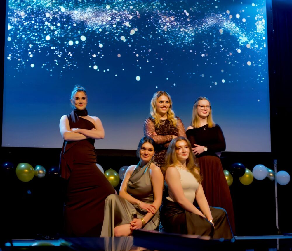 Fünf Schüler*innen der Q2 in festlicher Abendgadrobe stehen während des Varietéabend auf der Bühne und blicken ins Publikum.