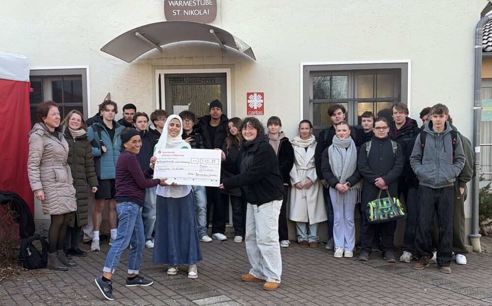 Schüler:innen der Religionskurse des Herder-Gymnasiums mit dem Spendenscheck vor der Wärmestube St. Nikolai Minden - sehr zur Freude einer Mitarbeiterin