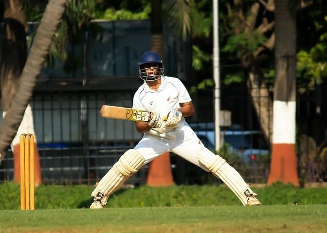 Cricket-Spieler in Sportdress und Helm und Schläger auf dem Cricket Platz